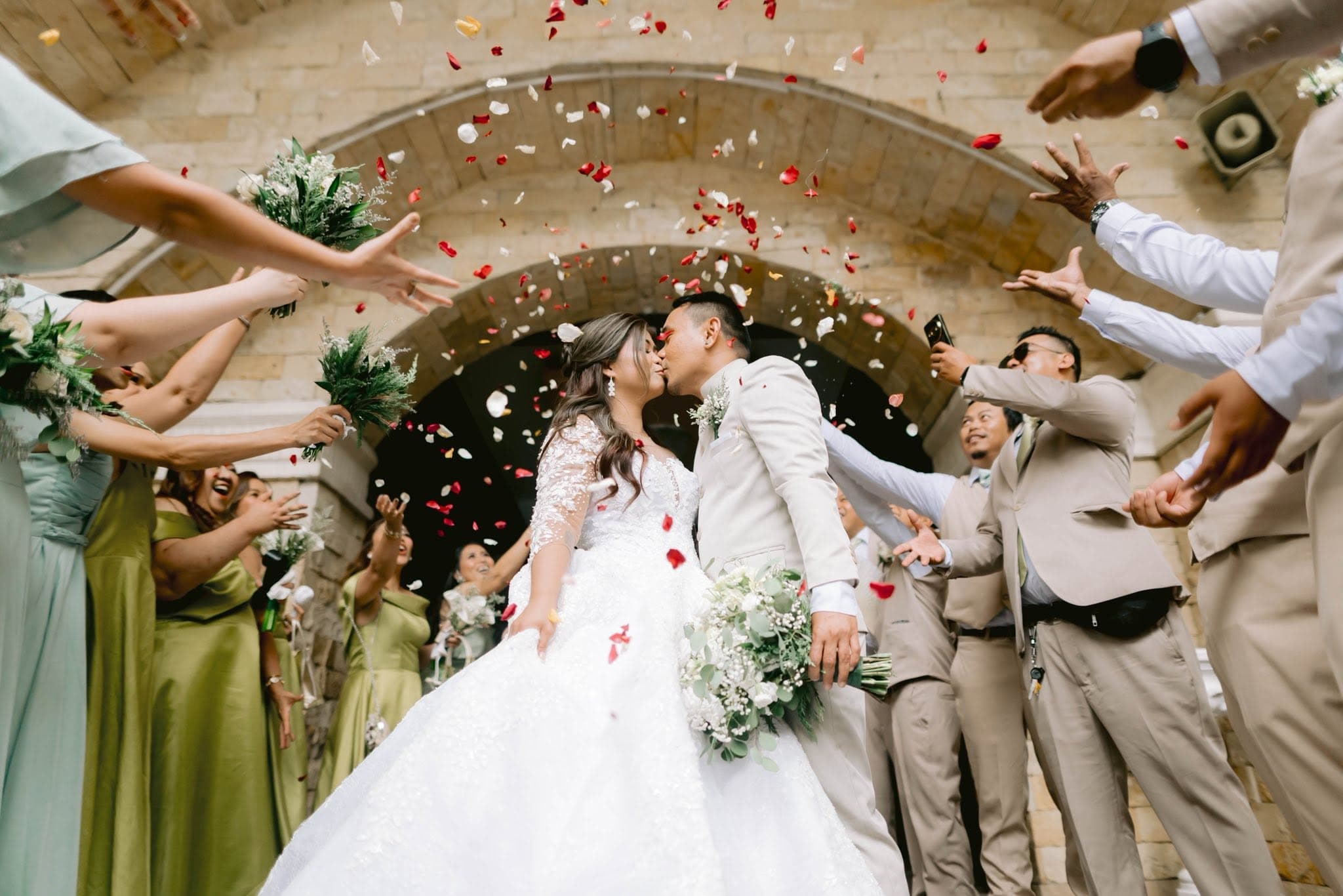 Augustus and Richelle kissing beneath a shower of petals as they leave the church