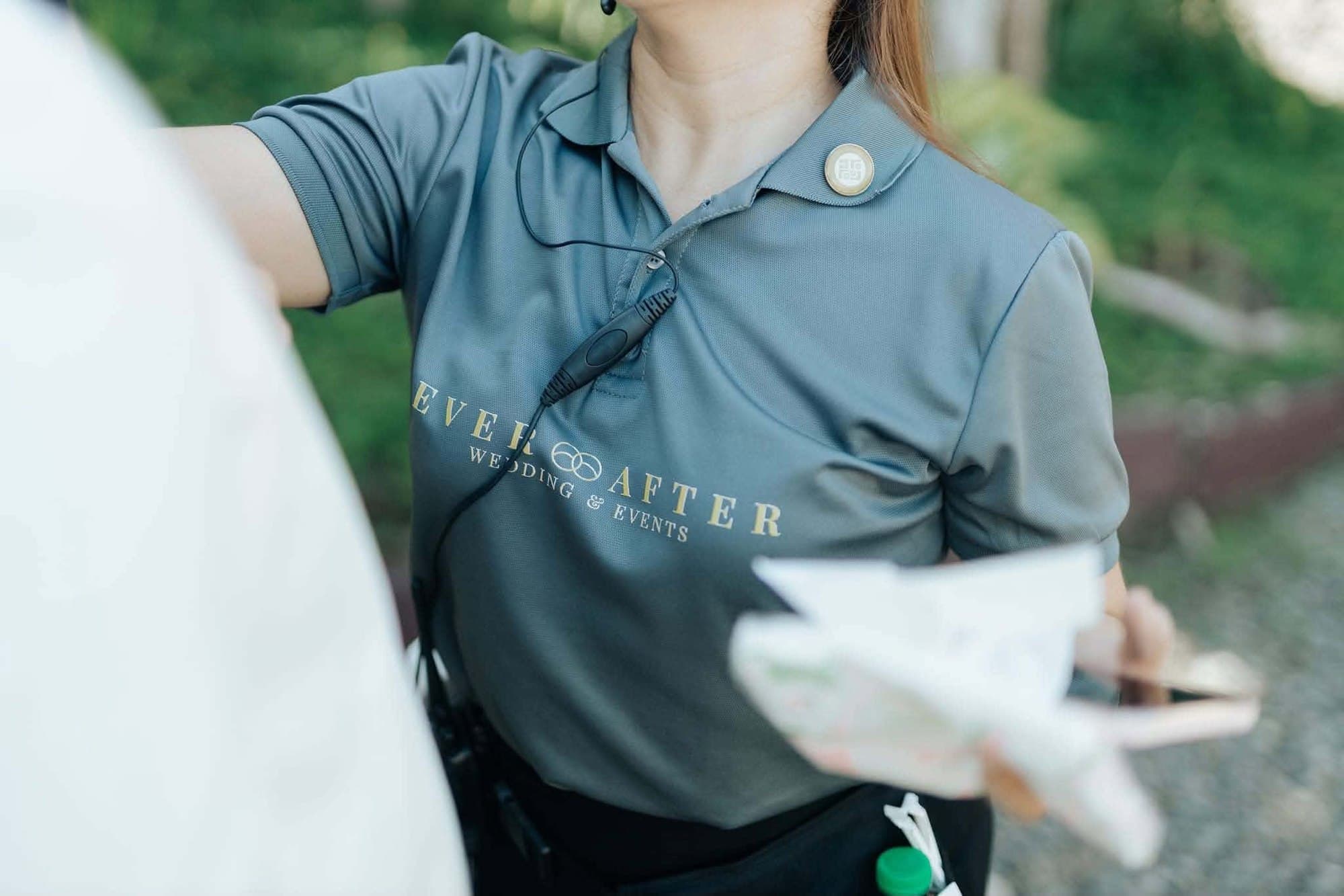 Close view of an Ever After branded polo shirt and headset microphone as a coordinator hands something over