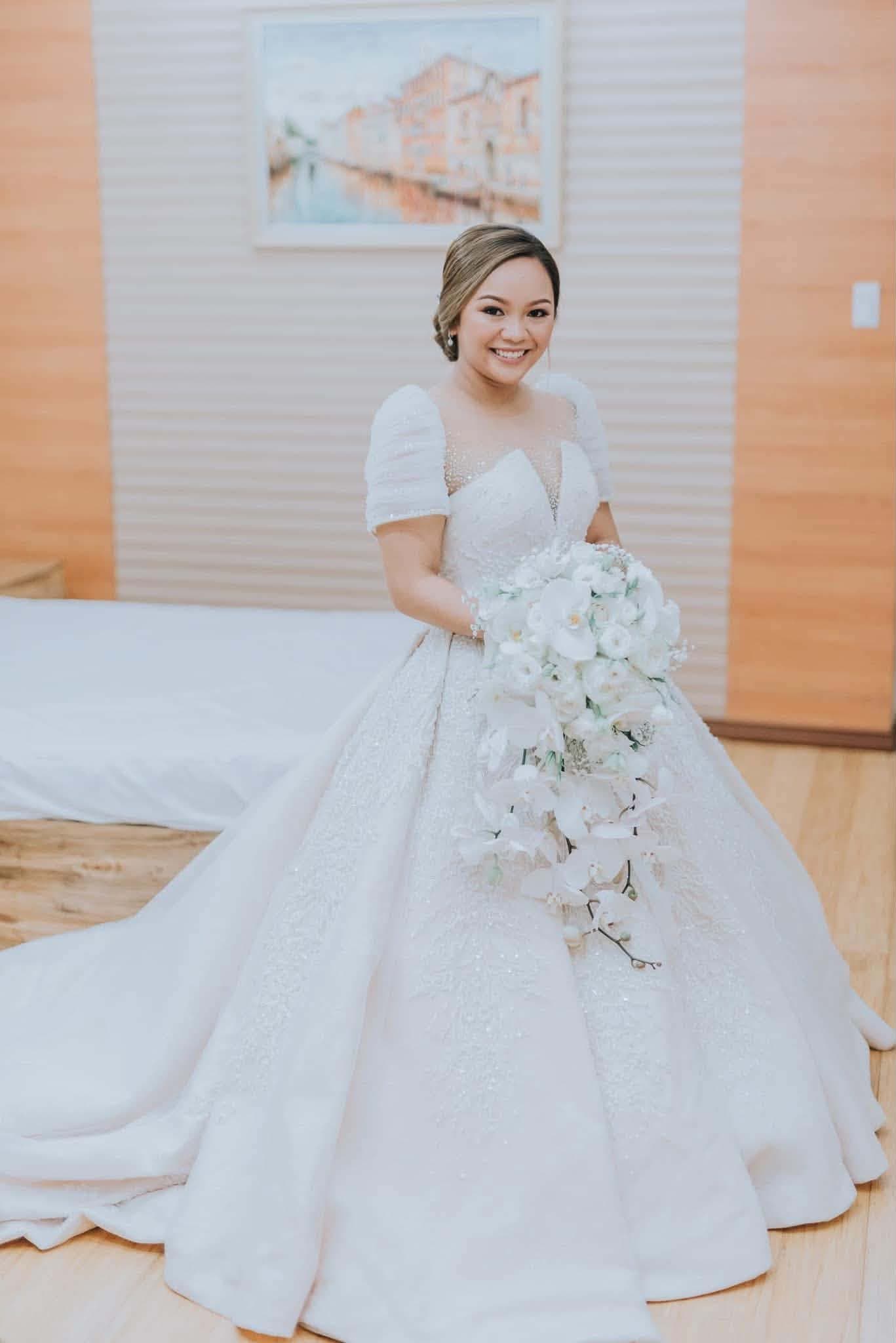 A bride in a beaded terno gown with a cascading bouquet of white orchids, her train spread across the floor behind her