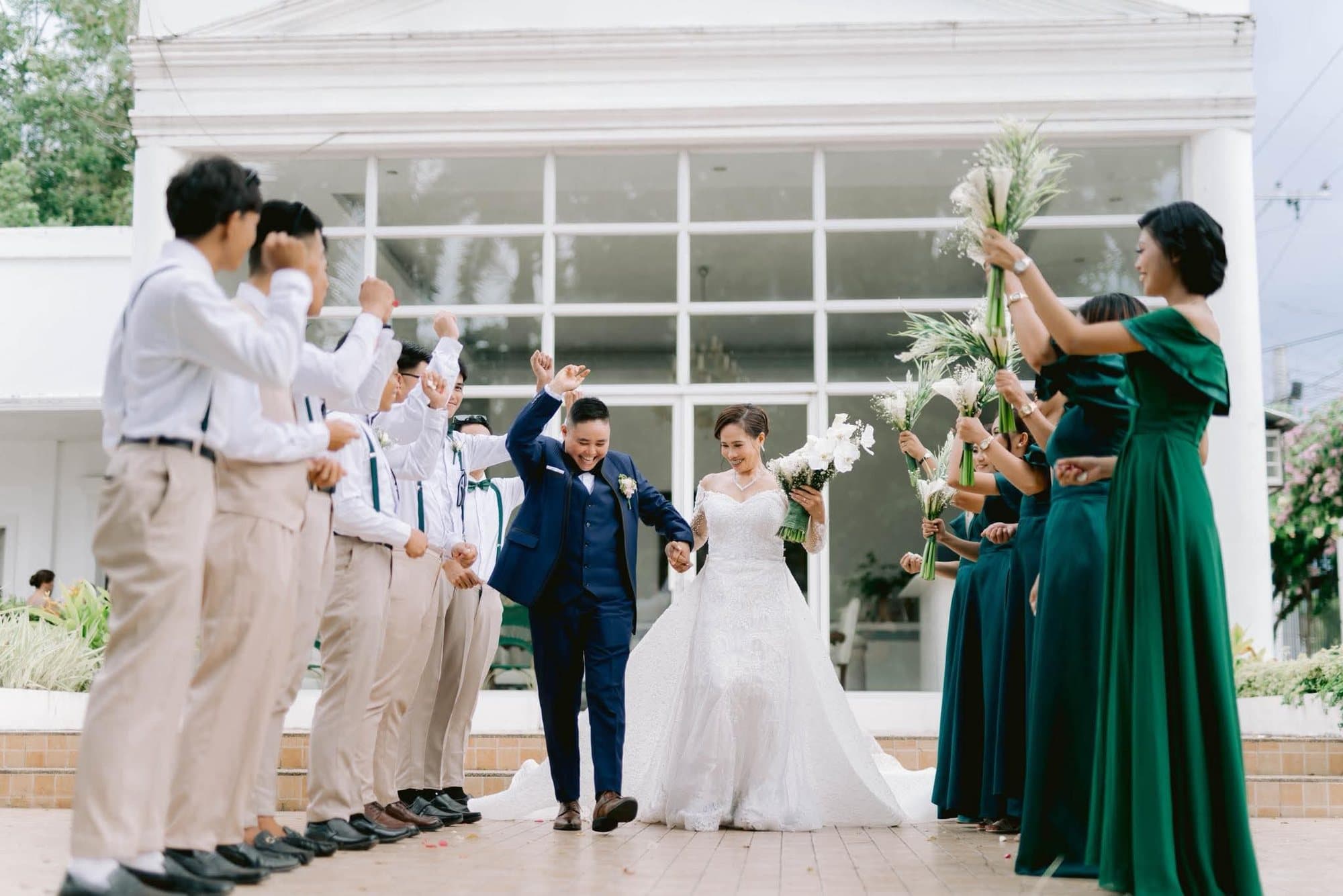 Newlyweds walking out hand in hand as their entourage raises bouquets overhead