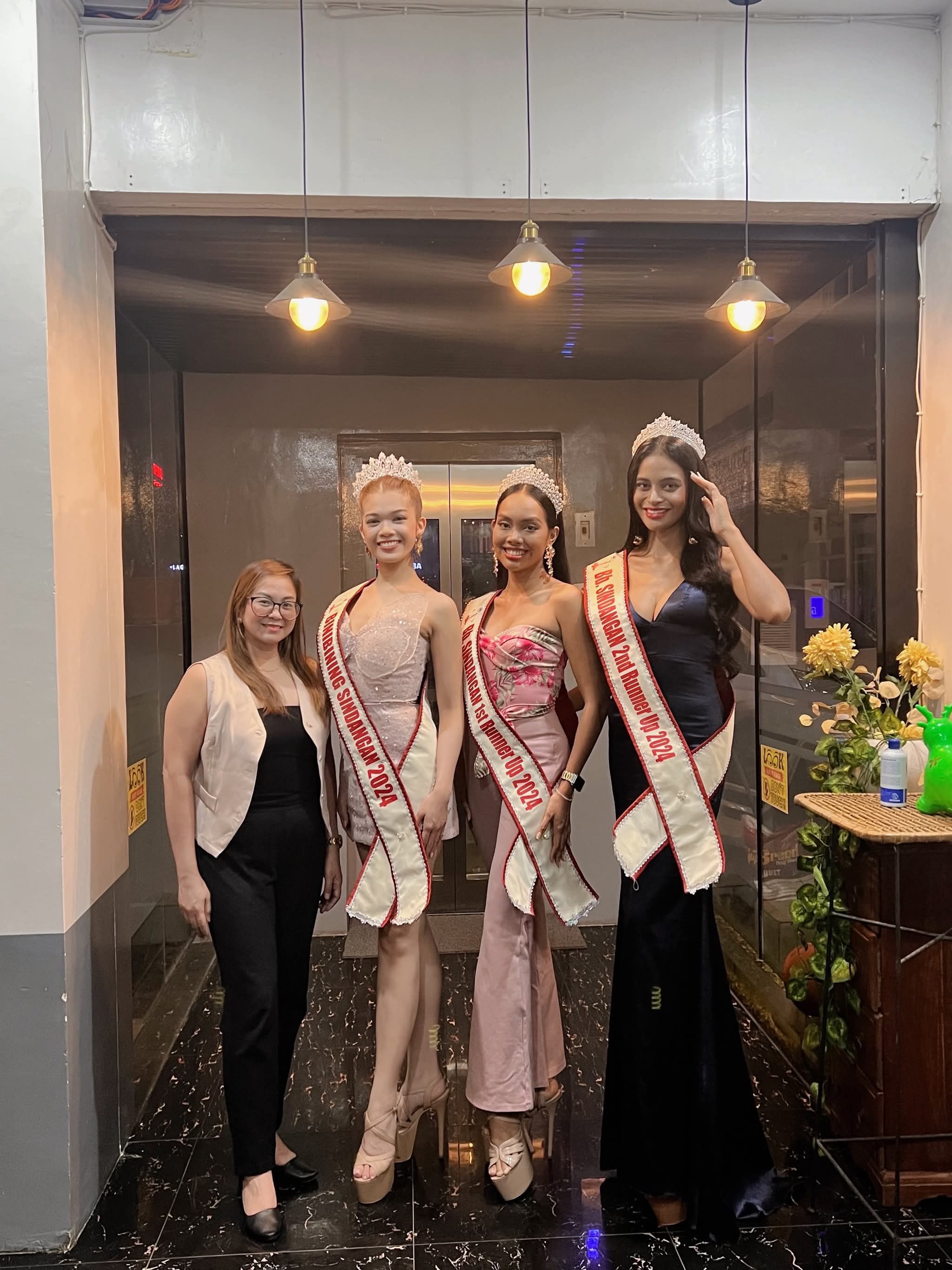A coordinator standing with three pageant titleholders in sashes and crowns after the coronation