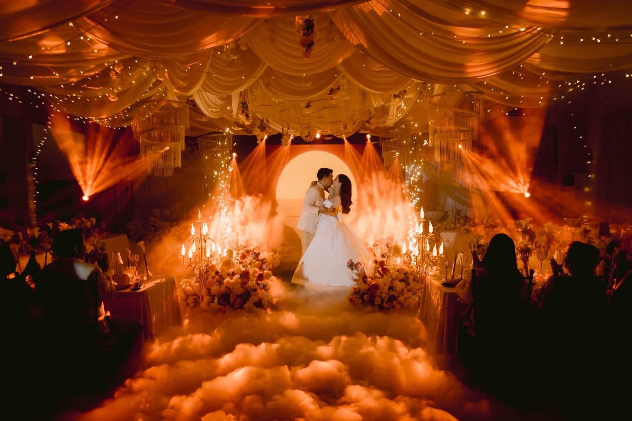 A couple kissing at the centre of a candlelit reception, sparklers and low fog around them