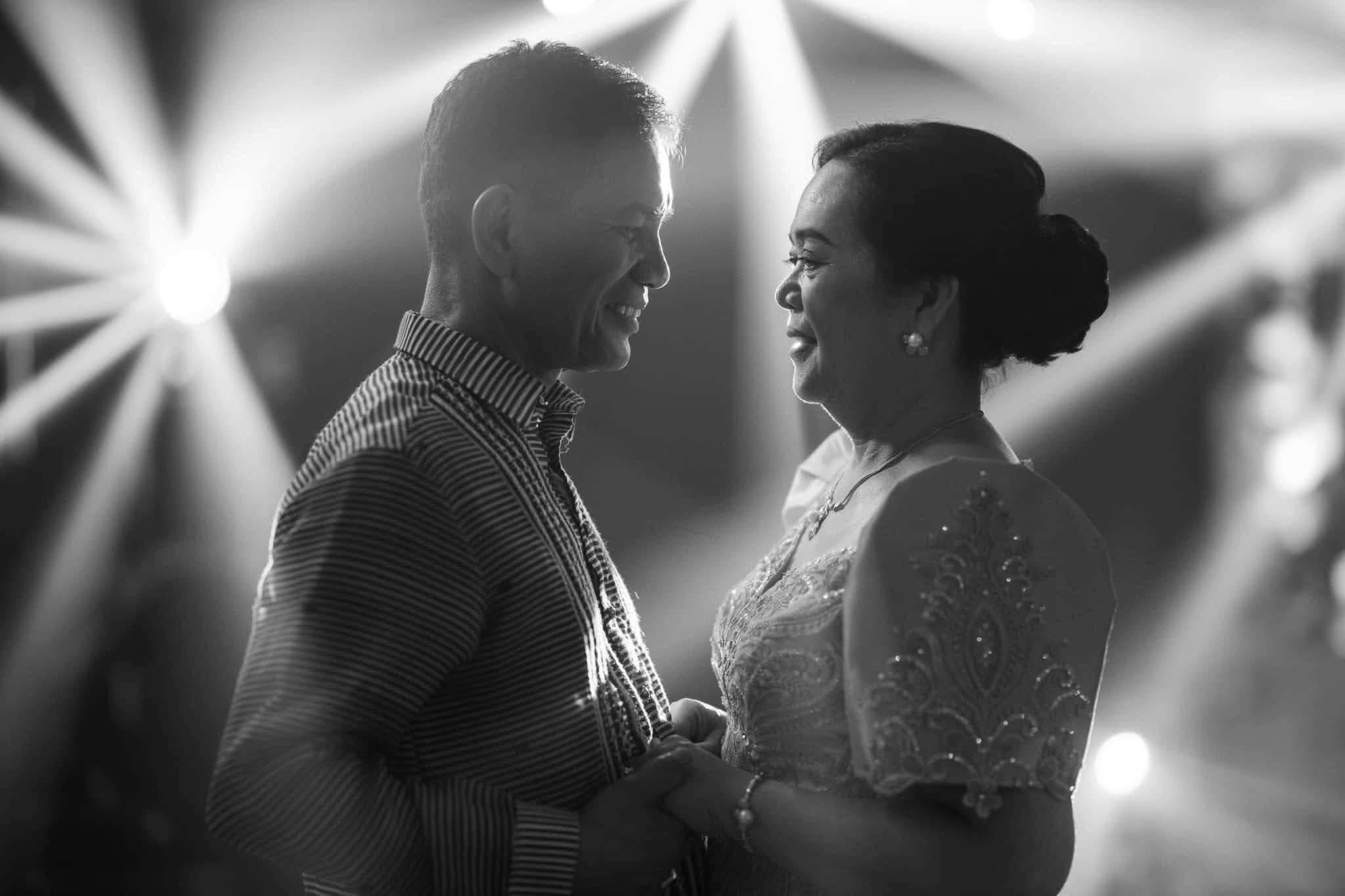 A couple facing each other mid-dance beneath starburst lights, in black and white