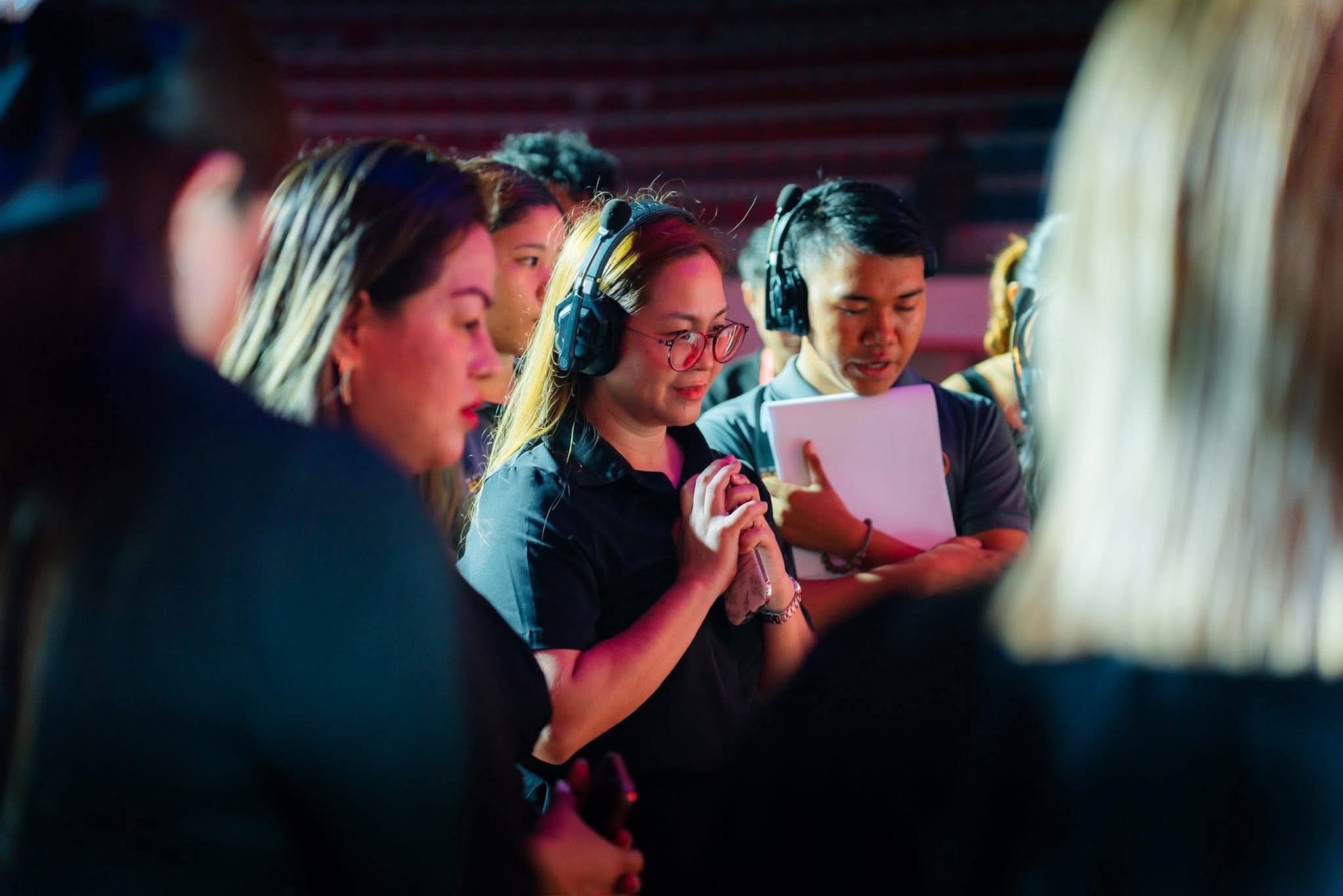 Coordinators in headsets standing together in a darkened venue, one with her hands clasped, another holding a run sheet