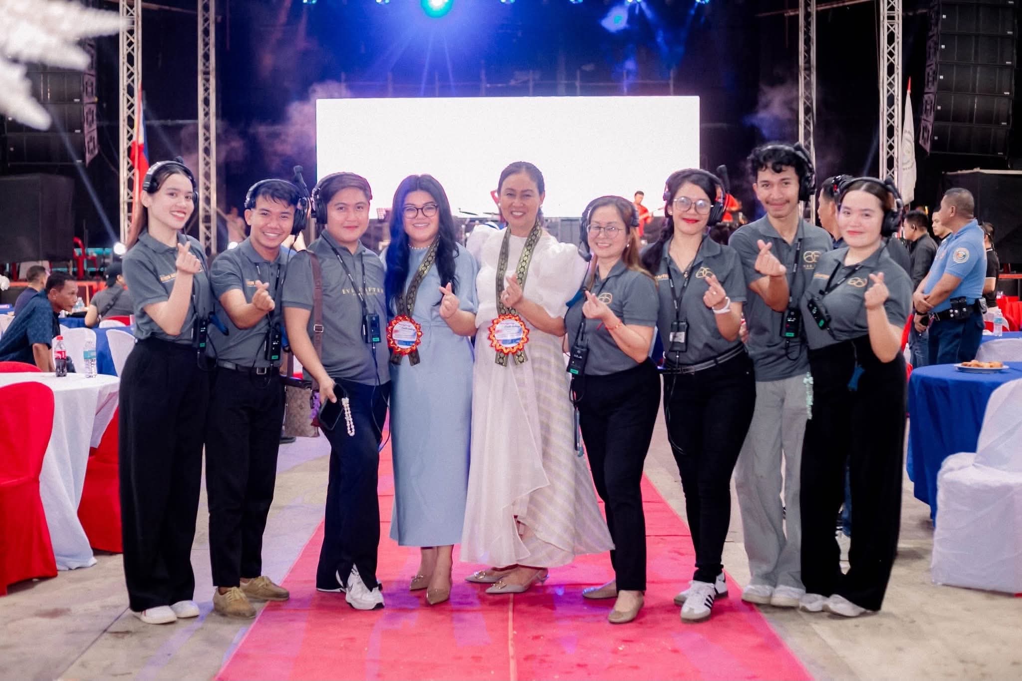 Seven coordinators in branded polos and headsets on the red carpet with two guests of honour, the stage lit behind them
