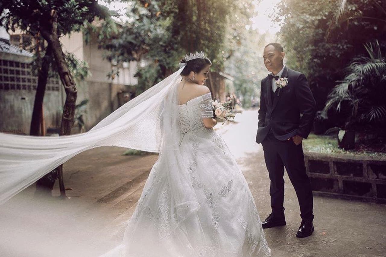 A bride's veil lifting in the wind as her groom waits ahead