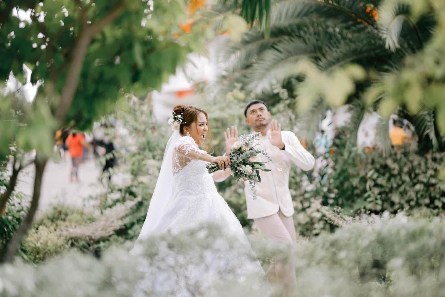A bride laughing with her groom among garden greenery, bouquet in hand
